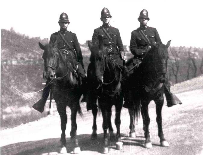 Black and white photo of three men on horseback and wearing coal and iron police uniforms and helmets